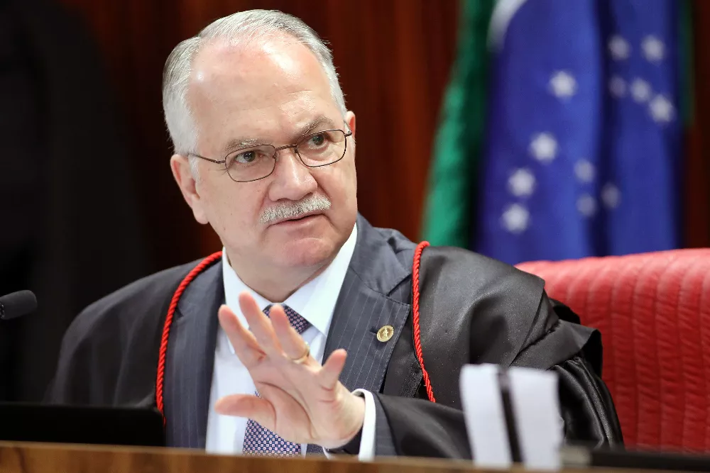 Em pouco mais de 48h, povos indígenas podem perder os meios para sua sobrevivência 14 Ministro Edson Fachin, homem branco, com cabelo e bigode grisalhos, veste roupa preta e óculos redondos. Ao fundo está a bandeira do Brasil.