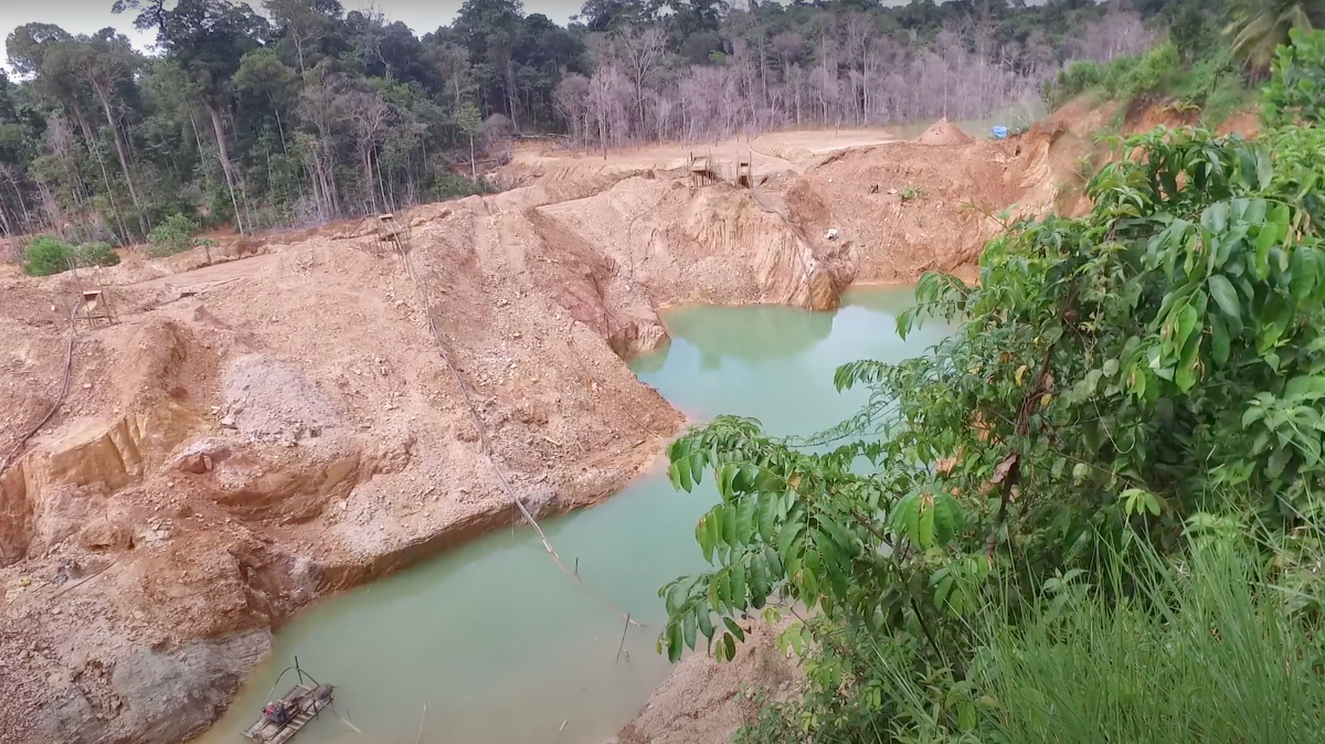 Imagem mostra área de exploração da garimpo, com montes de terras cavados e um pequeno poço de água escura e contaminada