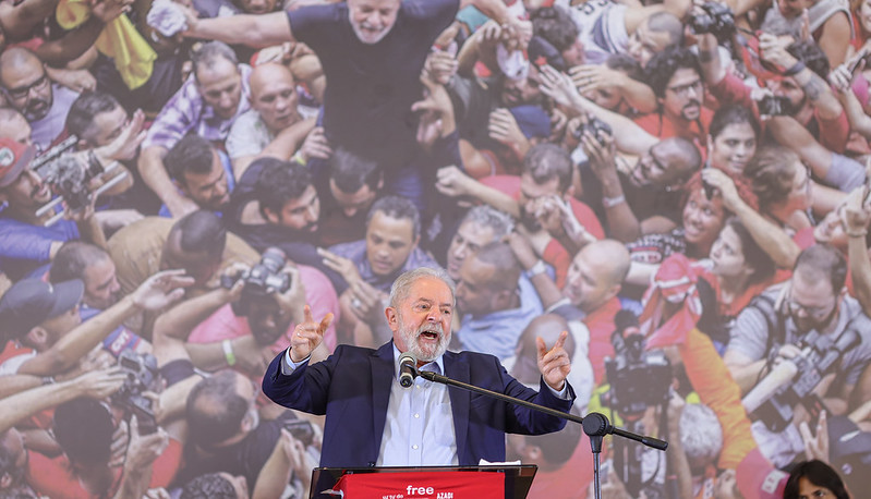 2022 e eleições: Lula vs Bolsonaro: desinformação e risco de golpe segundo pesquisadores 54 Enquanto gesticula com as mãos, o ex-presidente Lula tem uma imagem sua cercado por pessoas ao fundo
