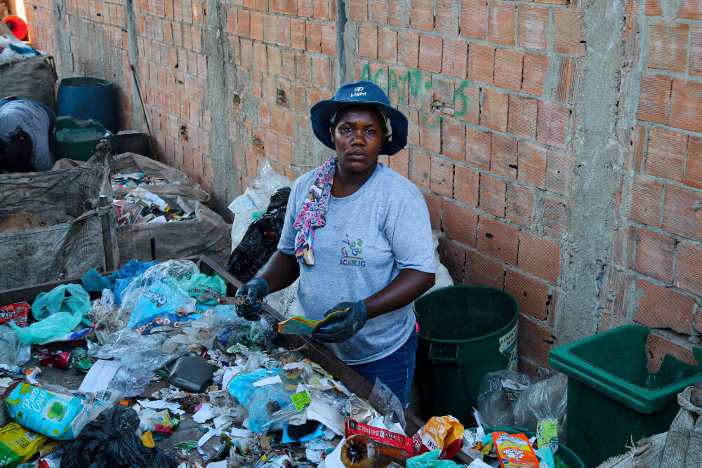 Roseane, é uma mulher negra de 35 anos; na imagem Roseana está manuseando descartes em um lixão